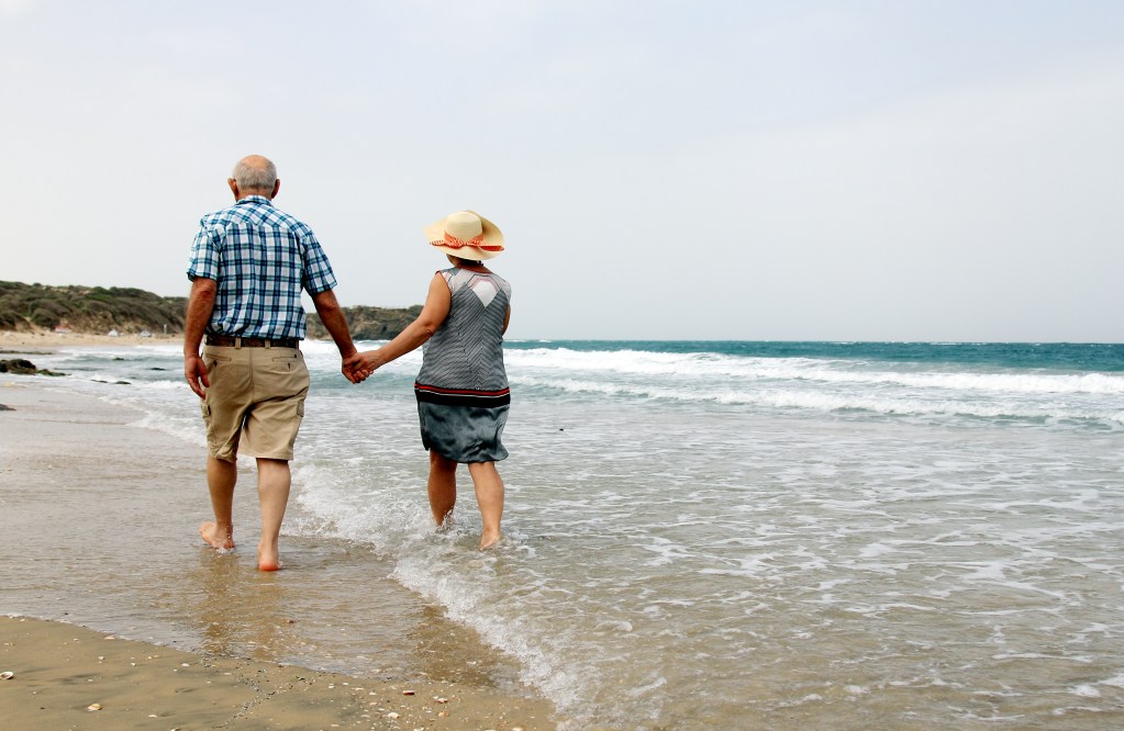 Una pareja de ancianos caminando de la mano por la playa, disfrutando del mar y el paisaje.